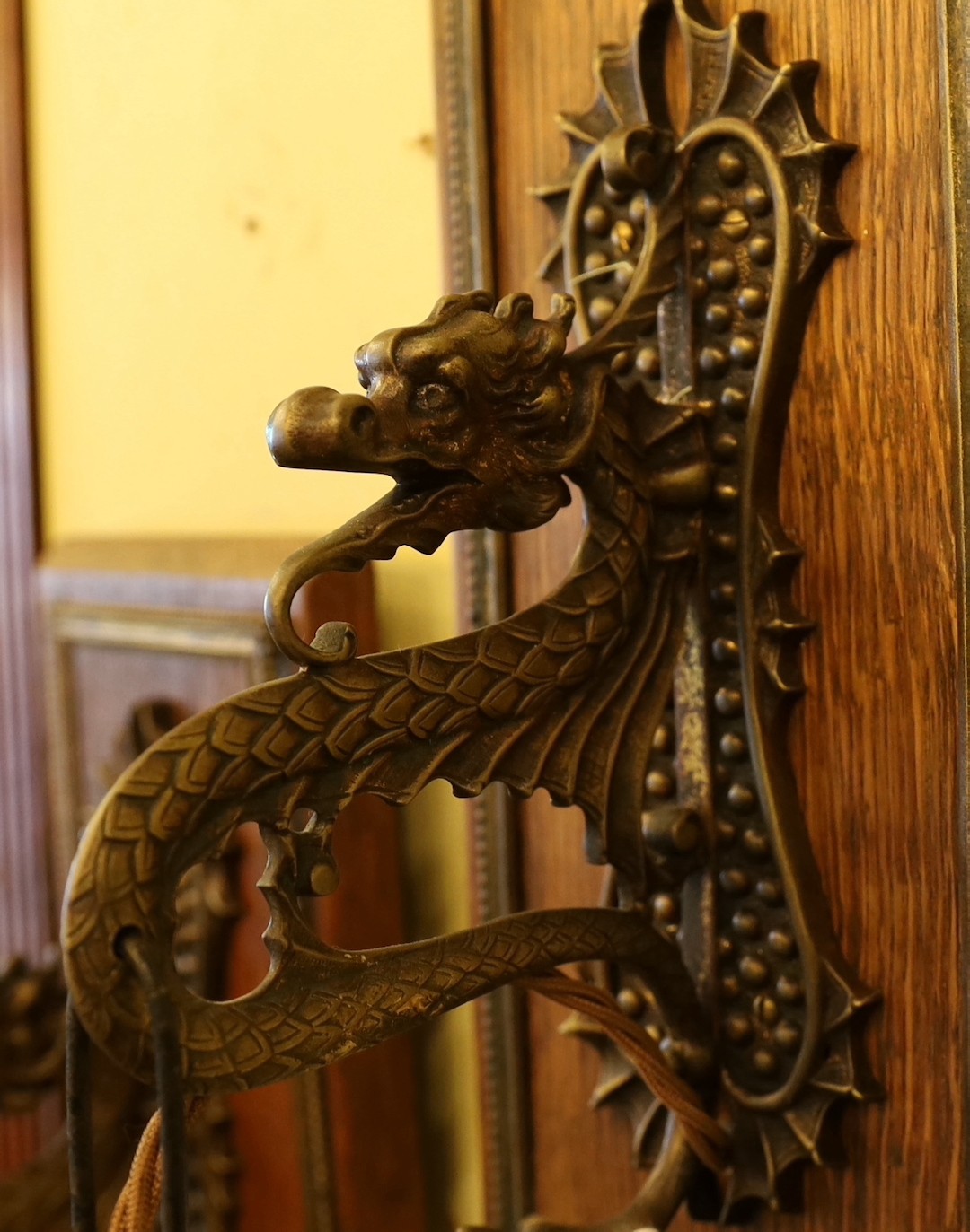 A pair of early 20th century English bronze metal dragon pendant wall lights, with moulded glass shades and mahogany back plates, height overall 35cm